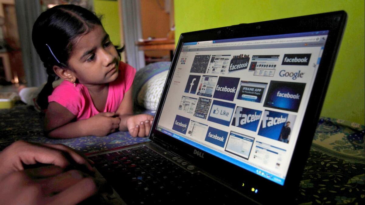 A child looks at a laptop displaying Facebook logos.