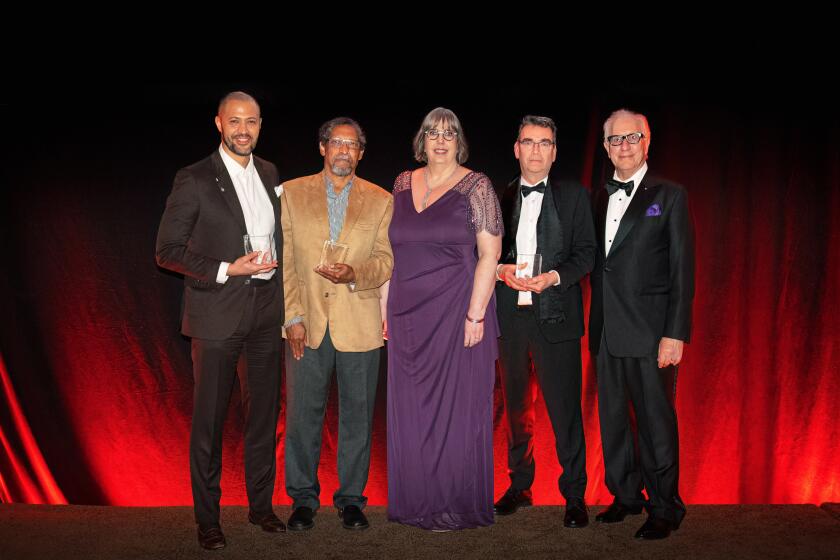 Four men and one woman in evening wear posing with awards in front of a red curtain.