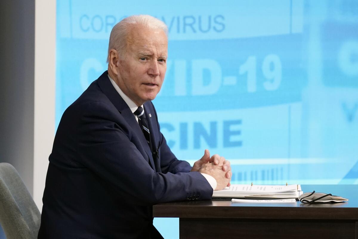 President Biden speaks before a blue screen that reads "COVID-19" 