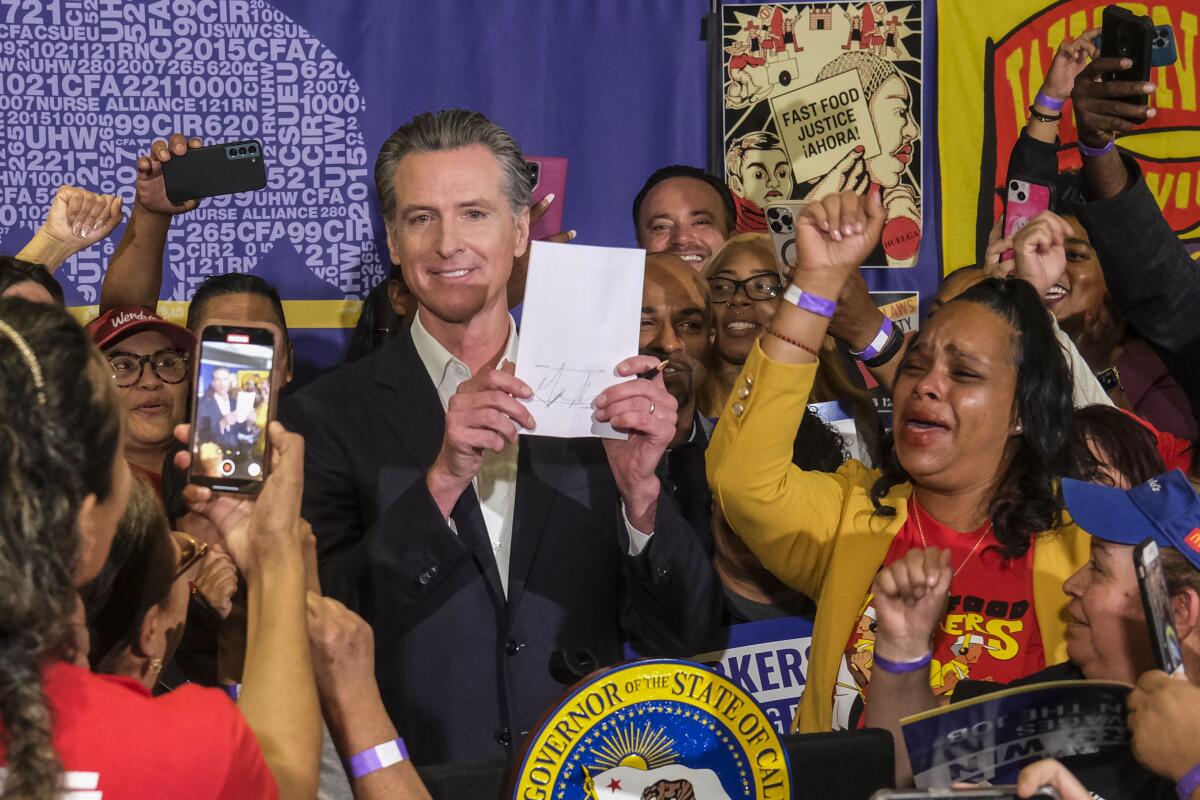 加州州长加文·纽森 (Gavin Newsom) 被快餐工人包围，举起一项立法 
