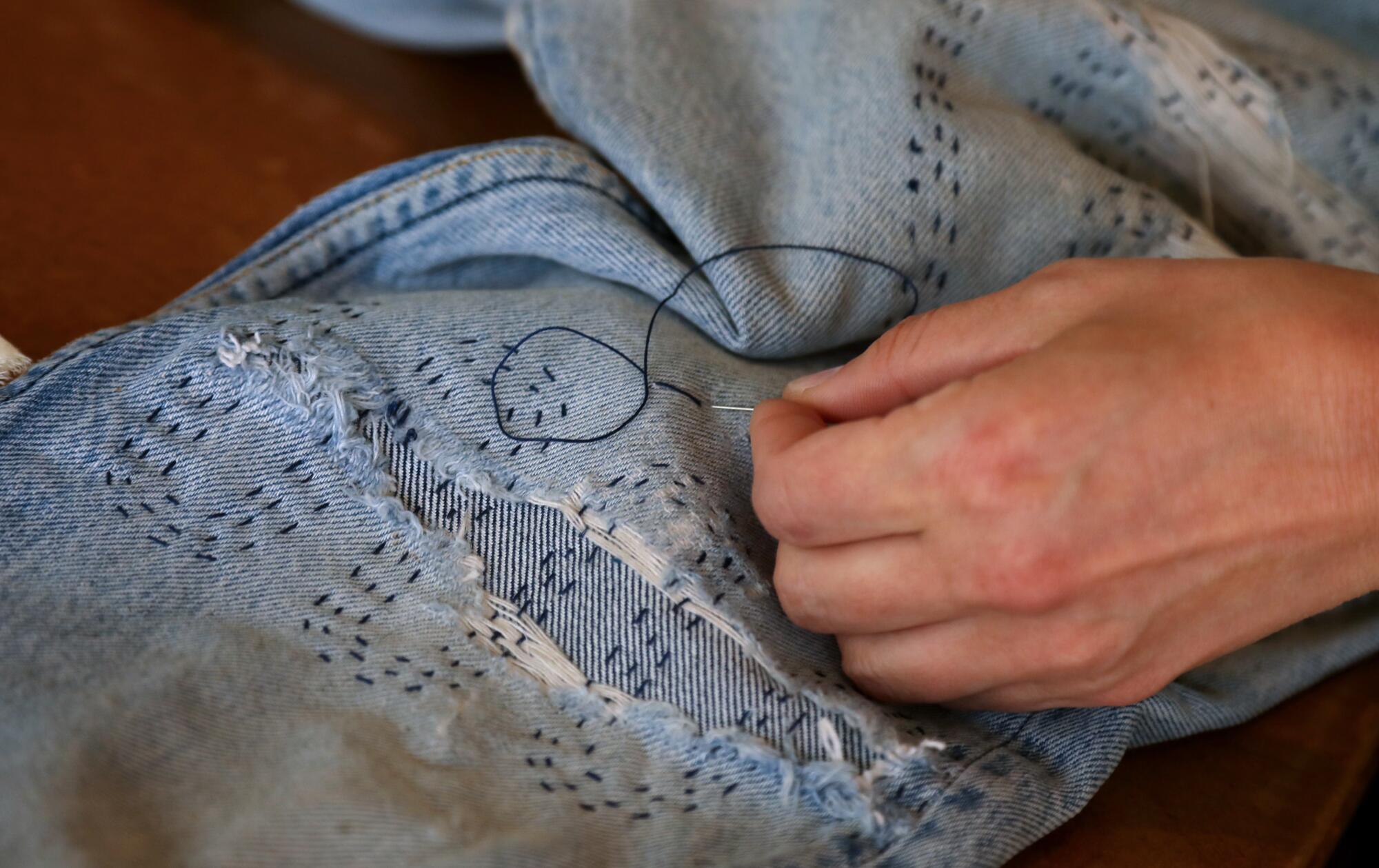 A close-up of jeans being hand-mended,