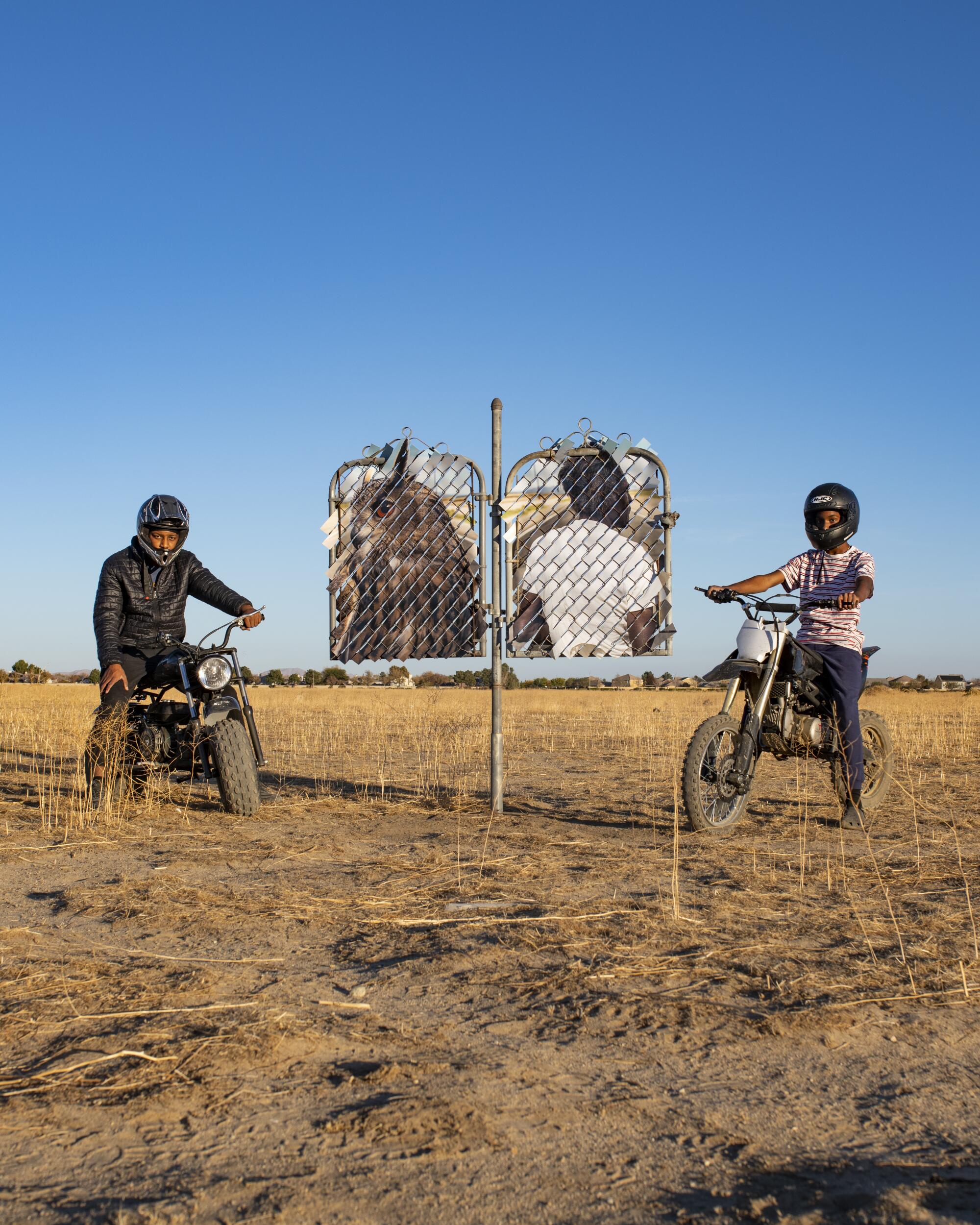 Two youths on bikes next to "Desert Totem (Lancaster, California)"