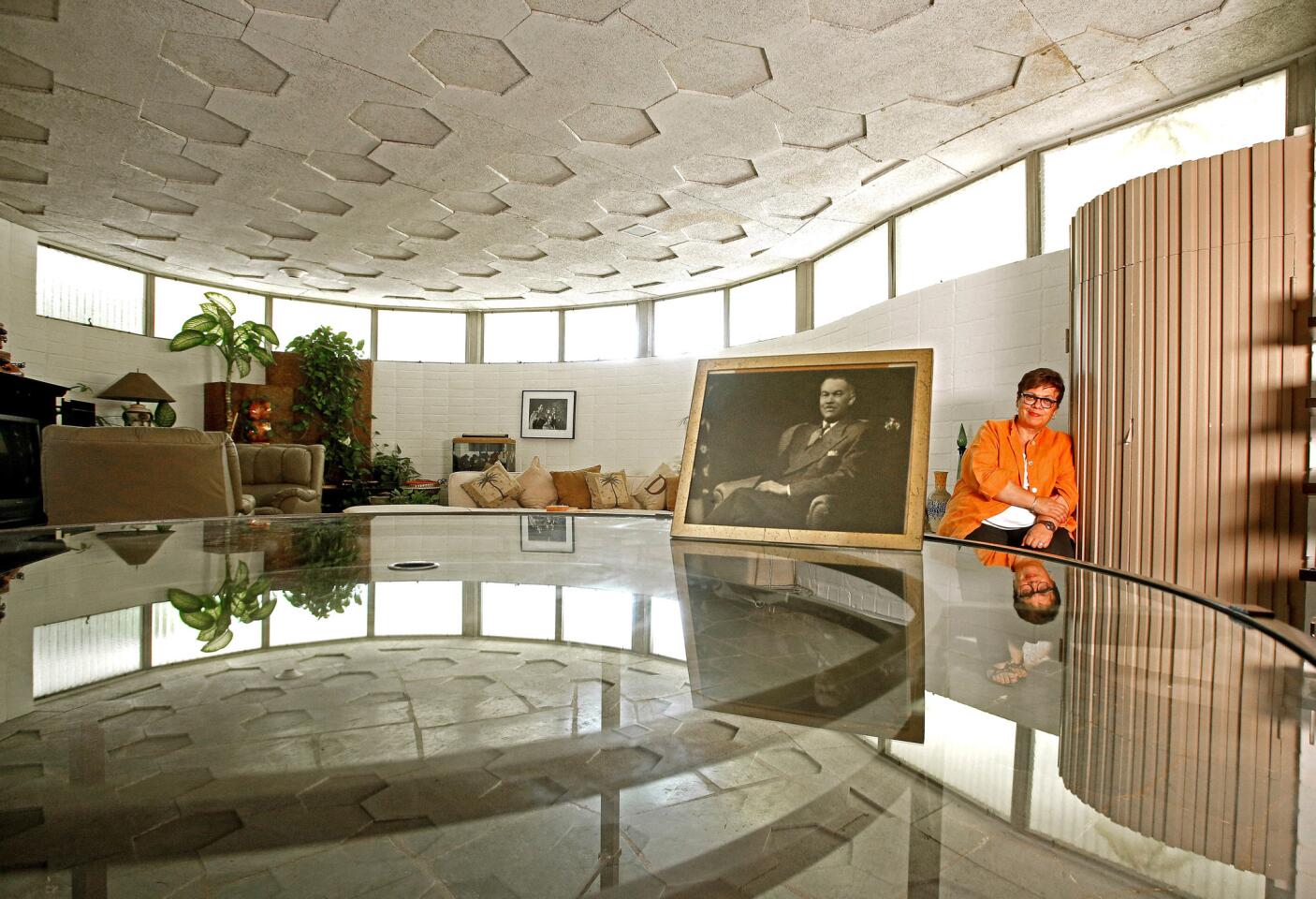 Karen Hudson sits in a curved lanai with a honeycomb roof before a photo of her grandfather, architect Paul R. Williams