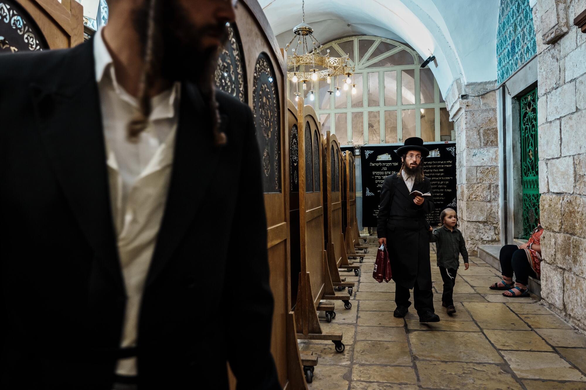 People in dark clothing and long beards walk along a stone-paved area inside a building