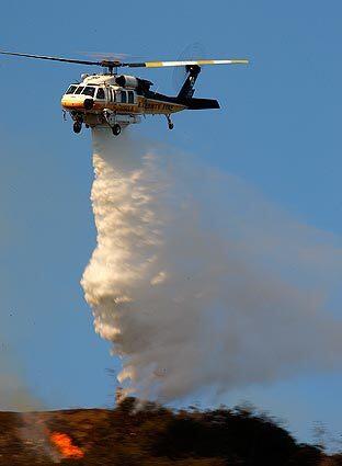 A Los Angeles County fire helicopter makes a water drop to help extinguish hillside flames as Los Angeles firefighters battle a blaze in the Sepulveda Pass.