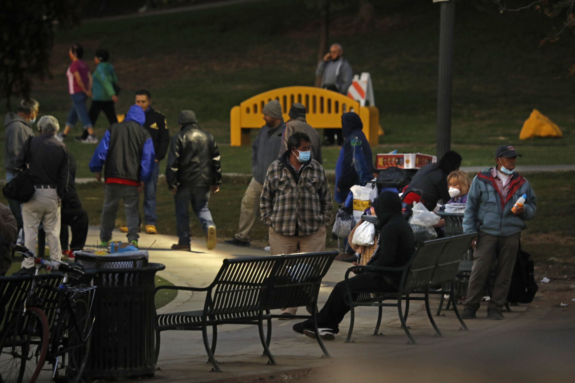 A crowd of people gathers on benches and a sidewalk under street lights at a park.