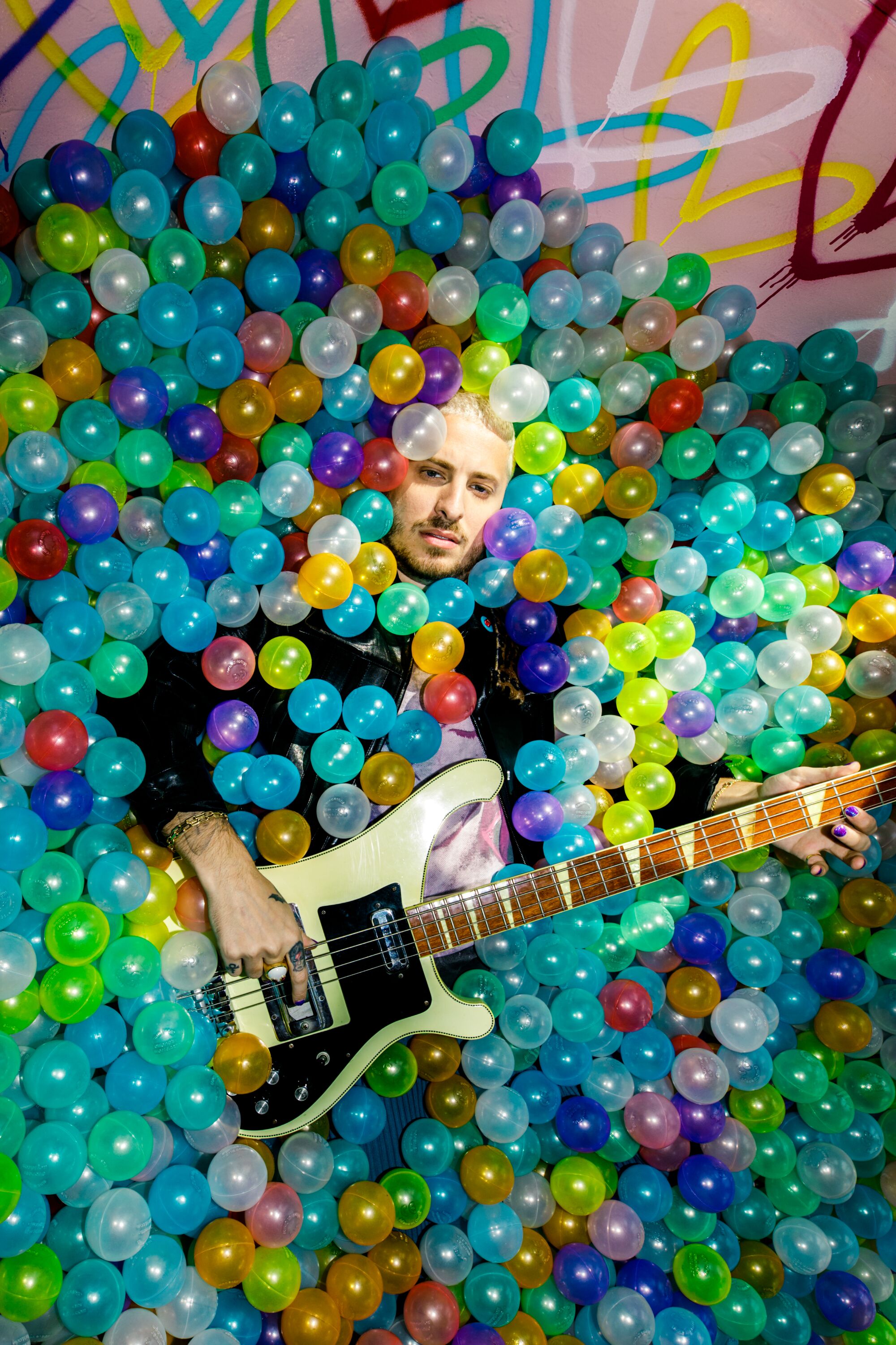 A man holds a guitar while in a colorful ball pit