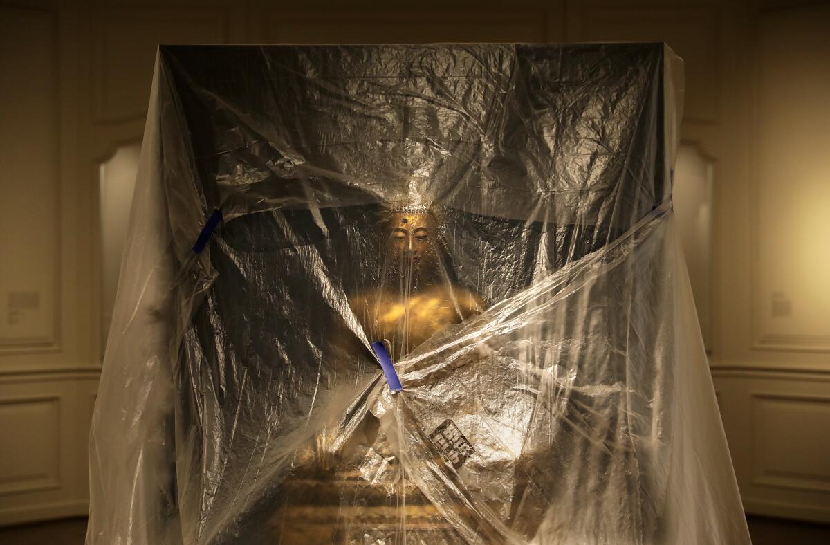 A view of a Buddha under clear plastic sheets in a gallery at the USC Pacific Asia Museum
