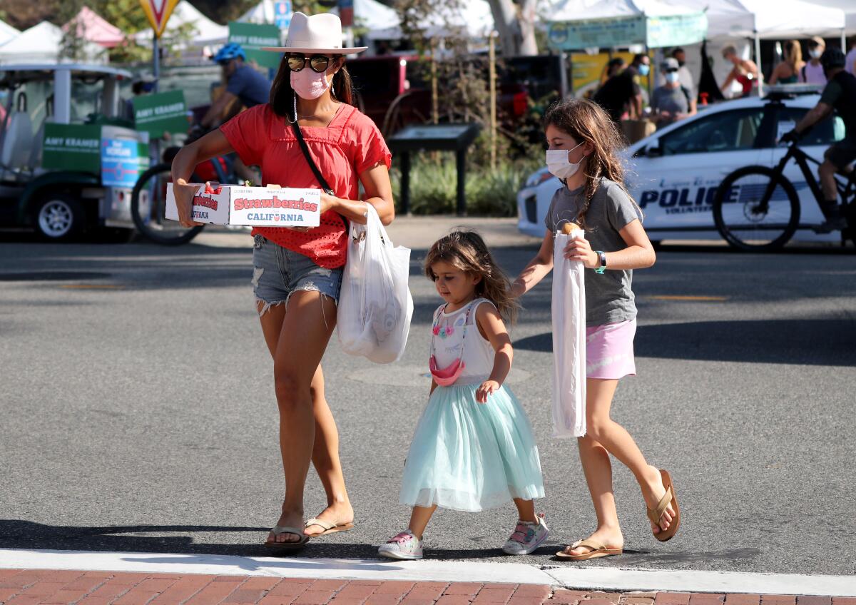 A woman and two children wear masks at the farmers market in Laguna Beach on Saturday.