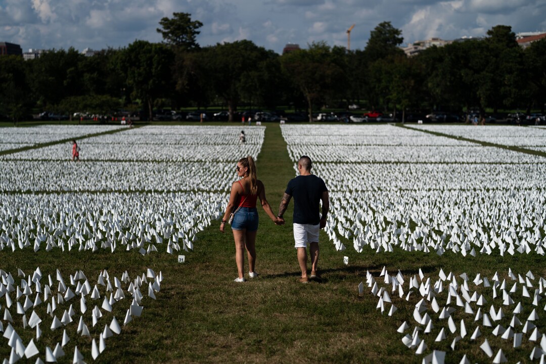 A couple hold hands walking between grids of small white flags in the grass