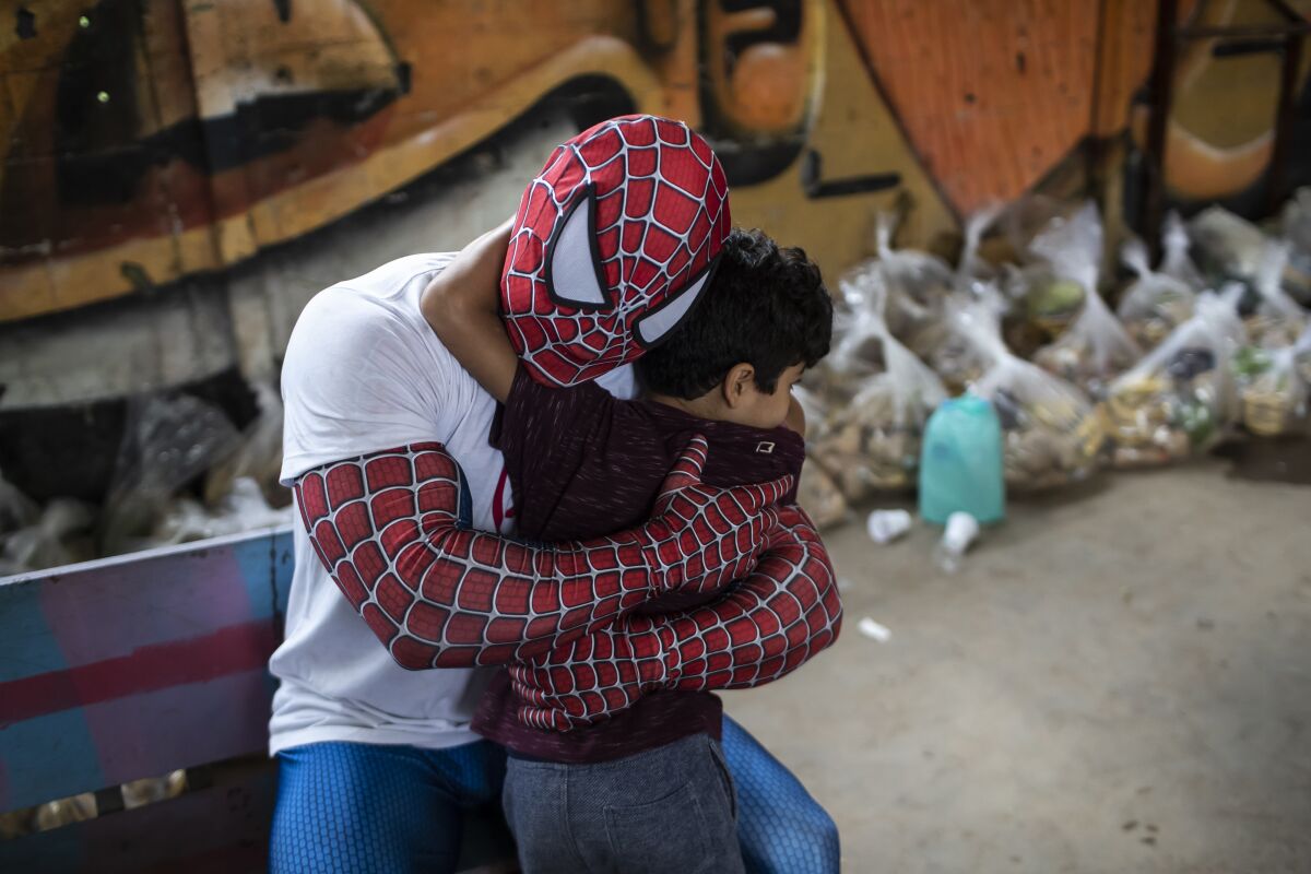 A volunteer dressed as Spiderman embraces a child in the Jardim Gramacho favela of Rio de Janeiro, Brazil, Saturday, Oct. 30, 2021, during a food kit delivery donated by the non-governmental organization "Covid Sem Fome" that works to fight hunger. (AP Photo/Bruna Prado)