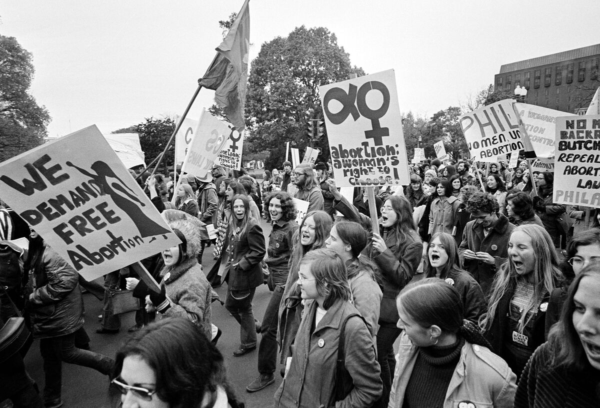A black-and-white photo of mostly women marching, with a sign in the foreground reading, "We demand free abortion"