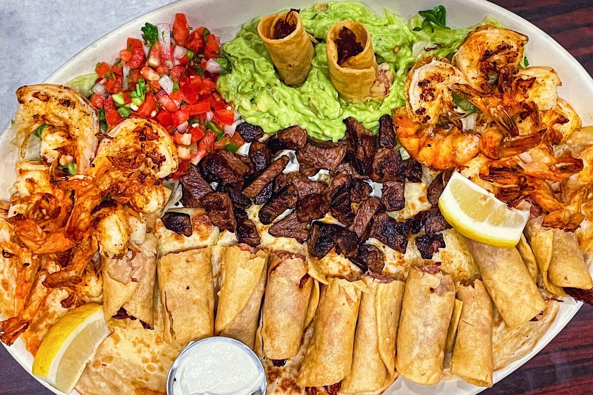 An overhead photo of a sampler platter, including taquitos, carne asada, butterflied shrimp, guacamole and pico de gallo.