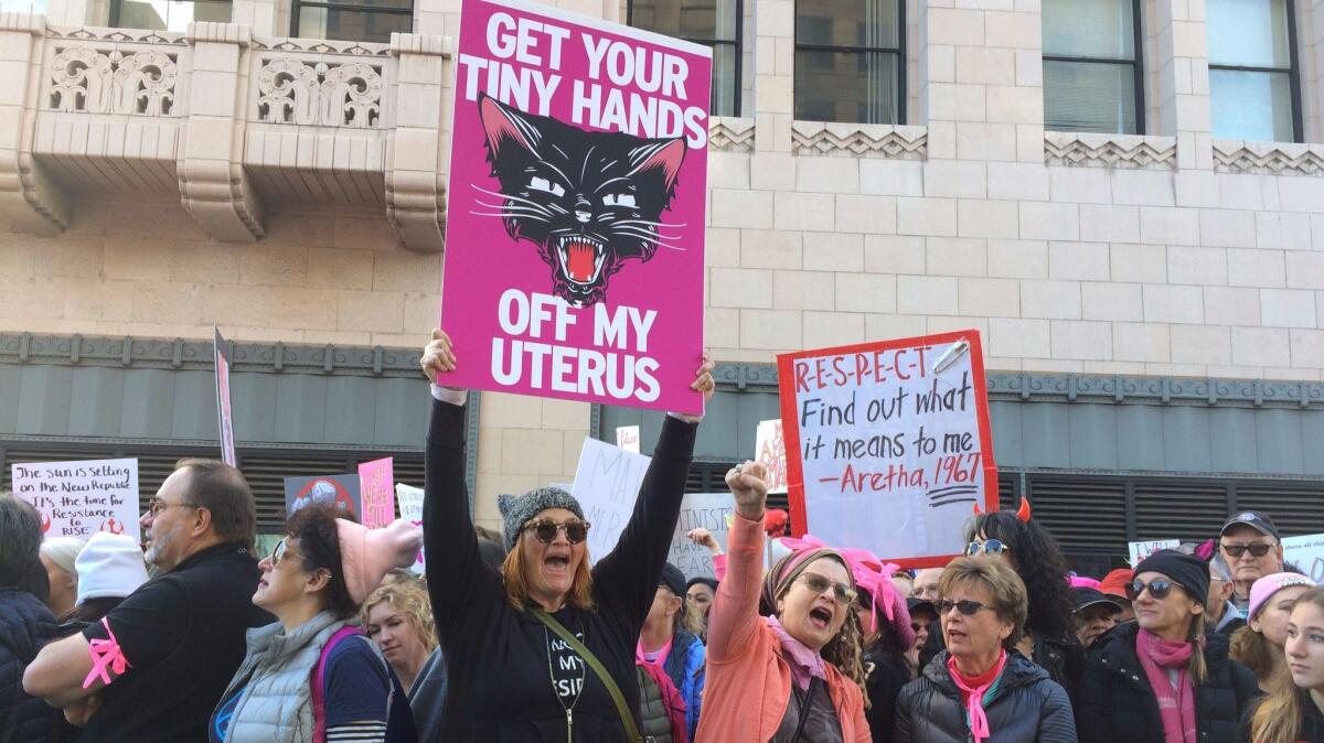 Arts publicist Heidi Johnson, in black, holds a protest poster designed by artist Sarah Ford at the women's march in downtown Los Angeles.