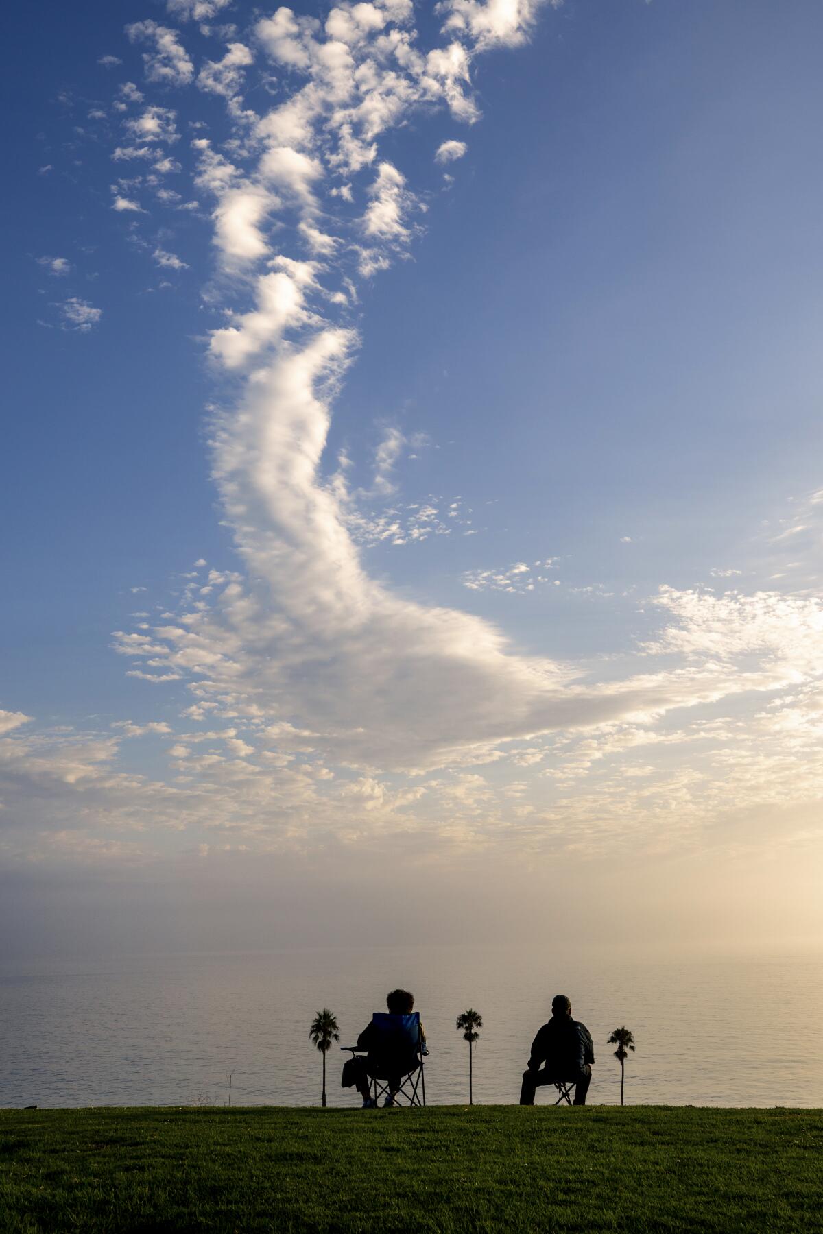 A couple relax in lawn chairs as they look out over the ocean.