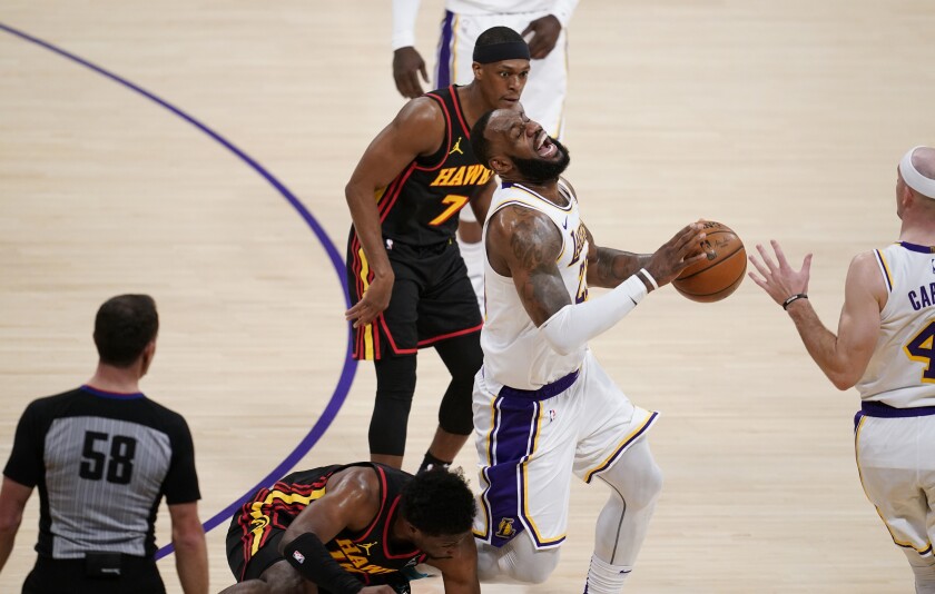 Lakers forward LeBron James grimaces as Hawks forward Solomon Hill crashes into his right leg.