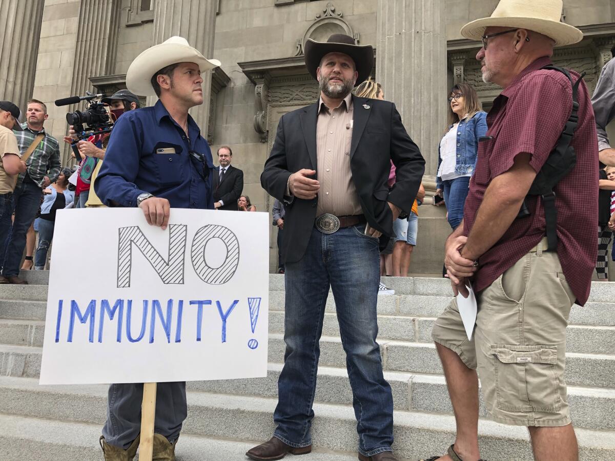 People in cowboy hats stand on steps of Idaho Capitol, one with a sign that says No Immunity