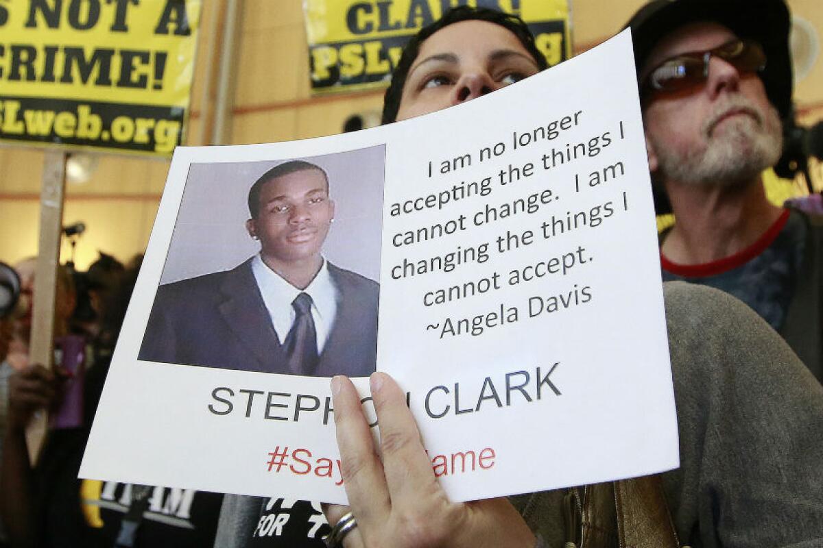 A woman holds a sign with a photo of Stephon Clark and a quote from Angela Davis