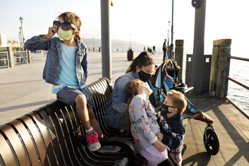 REDONDO BEACH-CA-FEBRUARY 10, 2021: Juliet Brown, 5, left, visits the Redondo Beach Pier with her siblings Evelyn, 7, and Joshua, 2, center, and their nanny Naomi Collicutt, on Wednesday, February 10, 2021. Wearing a cloth mask over a medical procedure mask can significantly decrease the spread of COVID-19, according to a new study by the CDC. (Christina House / Los Angeles Times)