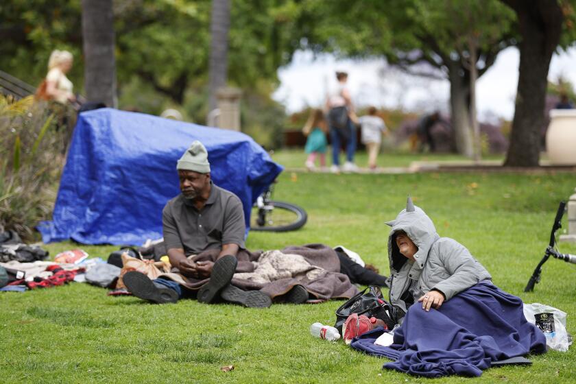 San Diego CA - June 12: Carey Edwards and Sabrina Johnson sit in the grass in Balboa Park on Monday, June 12, 2023. A proposal by the San Diego City Council would ban homeless encampments from some public areas such as parks. (K.C. Alfred / The San Diego Union-Tribune)