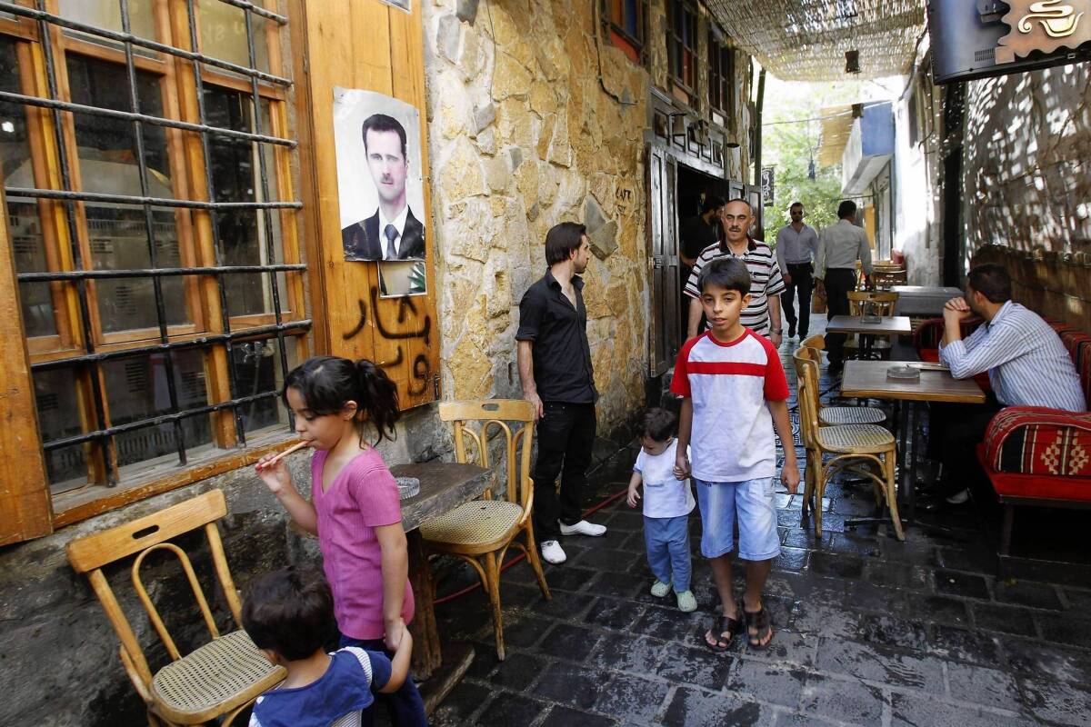 People make their way at a restaurant bearing a poster of President Bashar Assad in Damascus, Syria's capital. For residents, the routines of life continue, but the war is never far away.