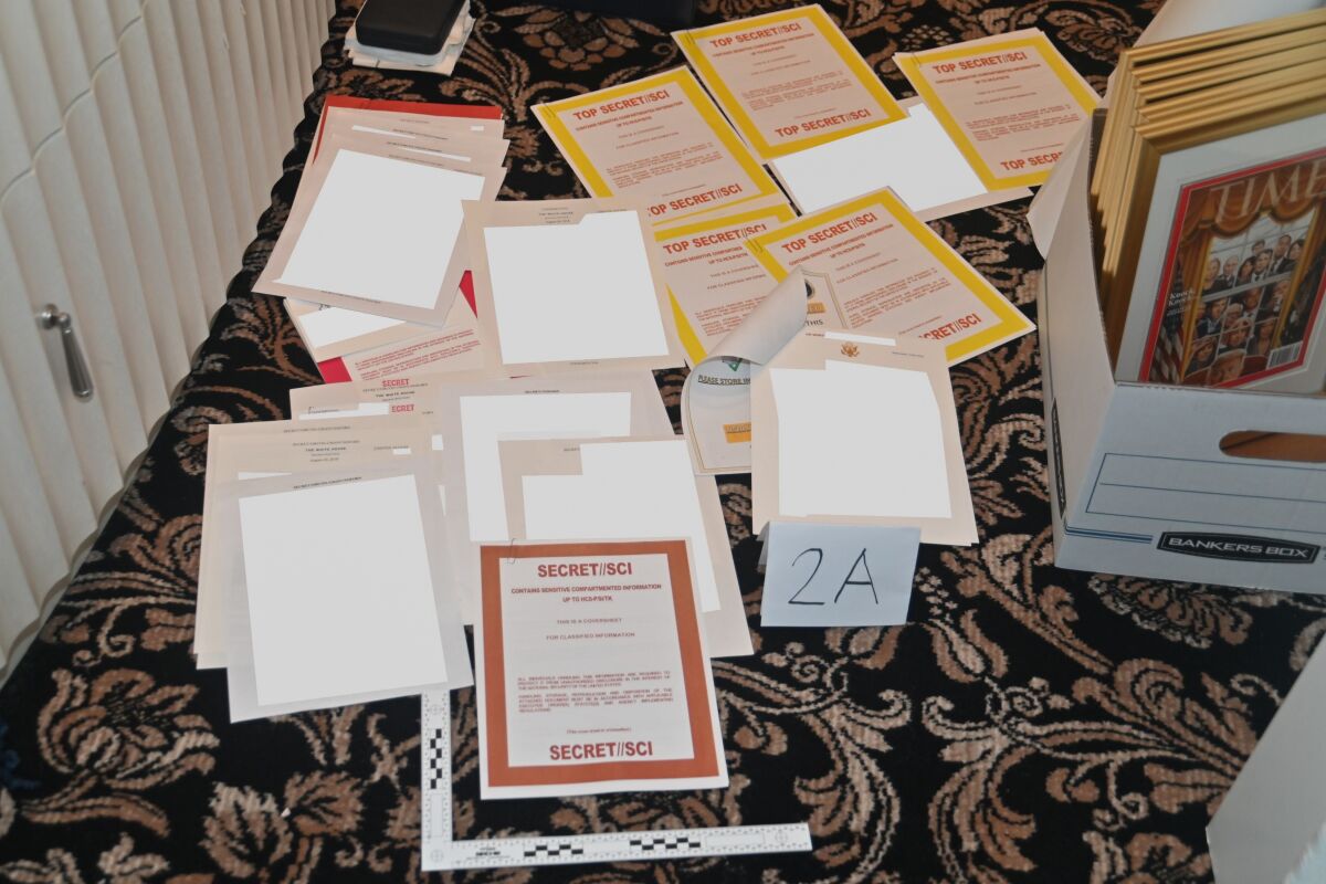 Papers marked "Secret" or "Top Secret" or obscured by white rectangles scattered on a floor next to a box of other items