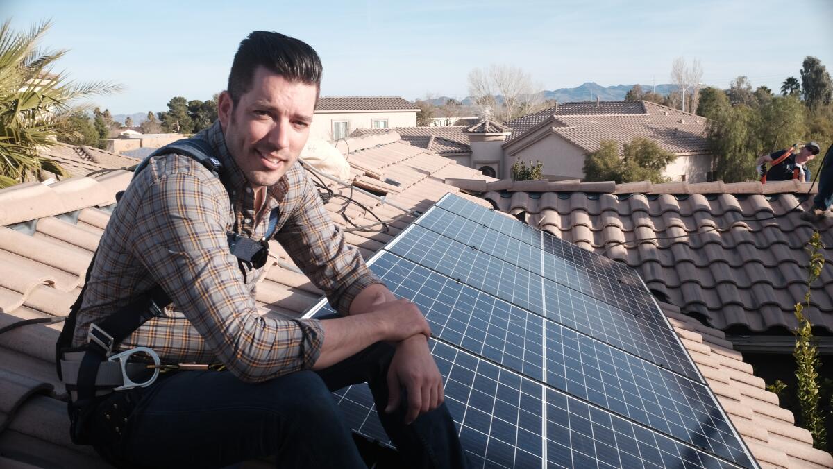Jonathan Scott sits on a tile rooftop next to solar panels