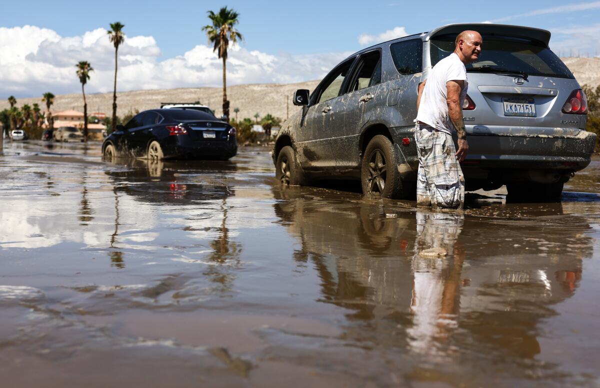 A man stands in the mud by a stranded car.
