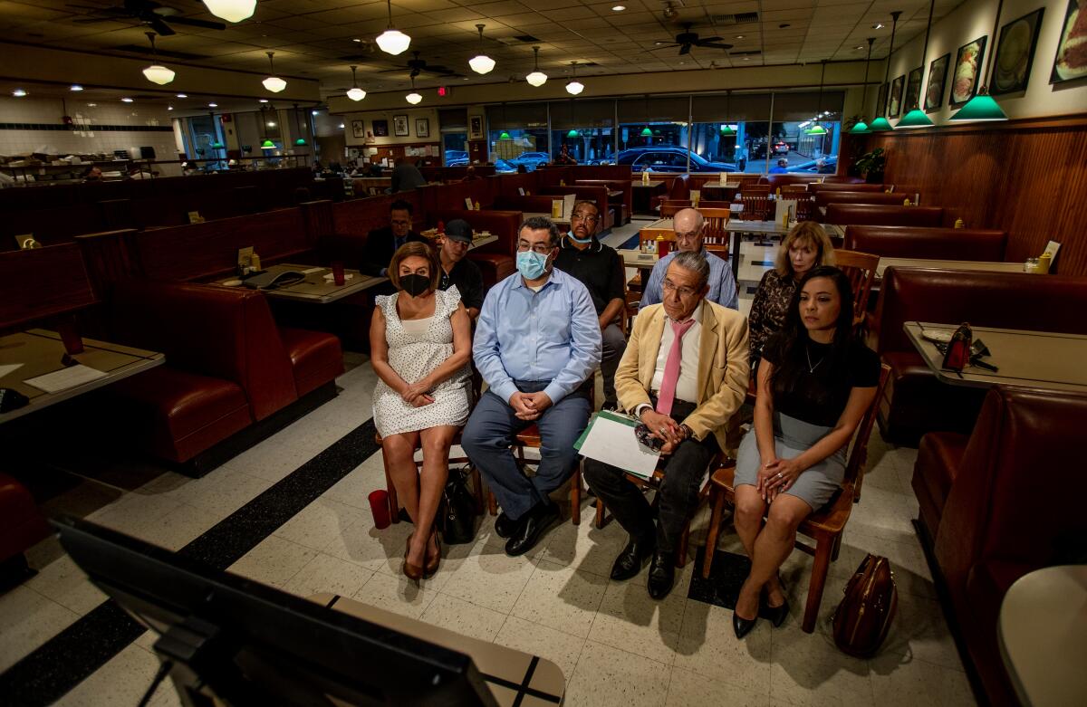 People sitting in chairs in a diner watch a TV monitor