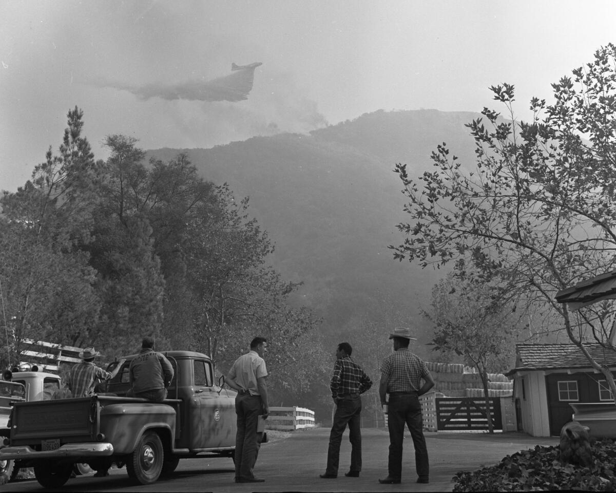 People watch an airplane fight a fire on a hillside