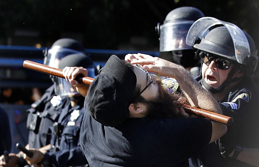 A police officer presses a baton against a man's neck.