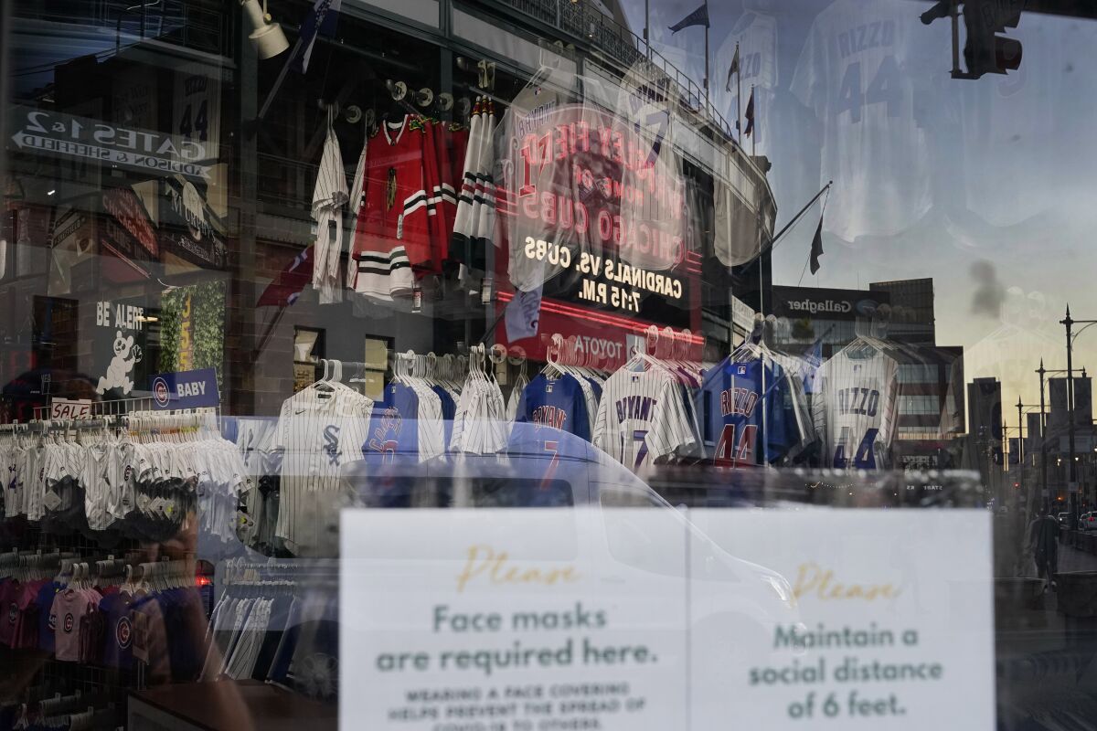 The Wrigley Field marquee is reflected Friday, Sept. 4, 2020, in the window of the Sports World apparel store in the Wrigleyville neighborhood of Chicago. The coronavirus pandemic has been especially hard on businesses that rely on ballpark traffic, eliminating crowds at major league games, and leading to rules that limit the amount of people they can have inside their doors at the same time. (AP Photo/Charles Rex Arbogast)