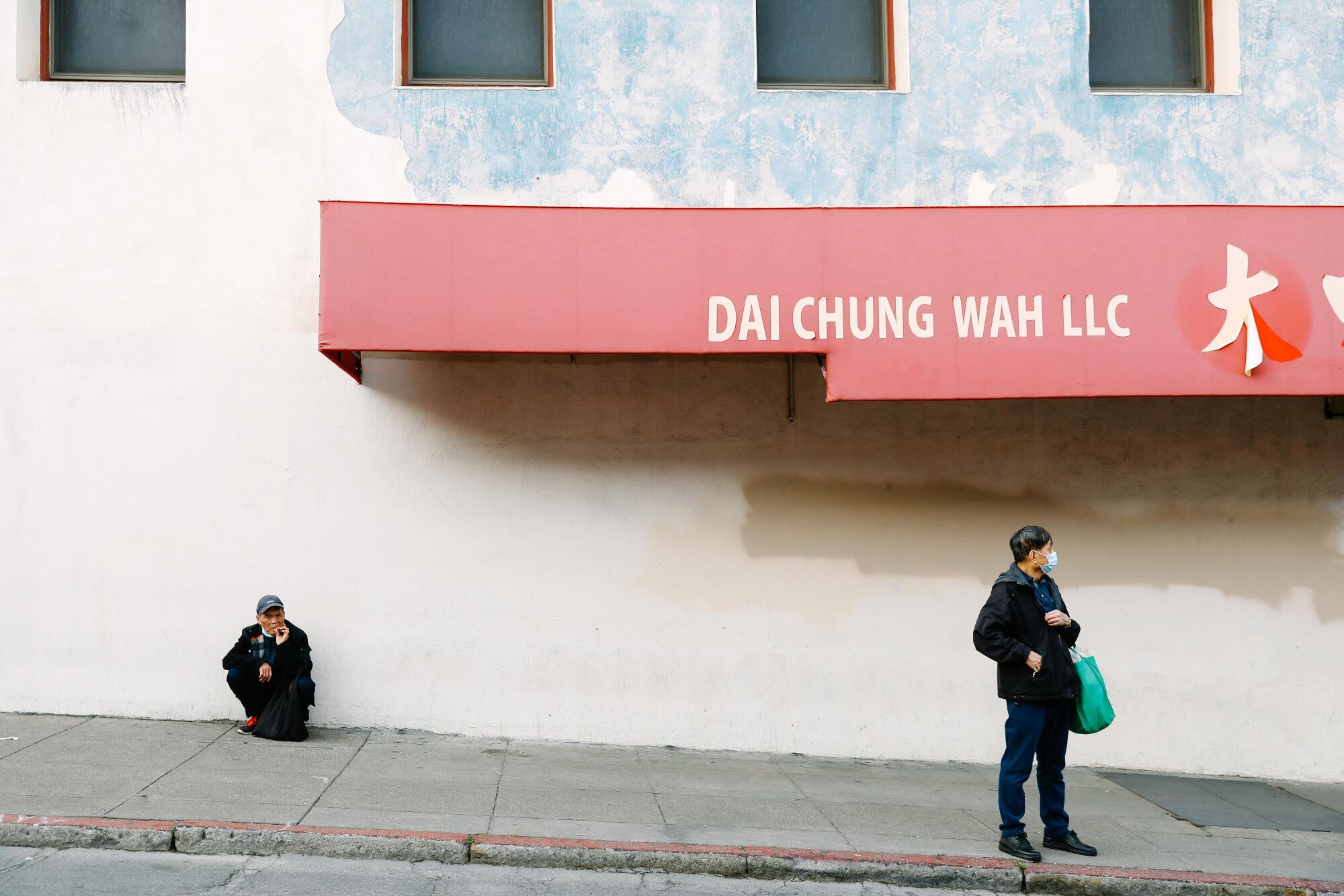 Two people wait on a sidewalk.