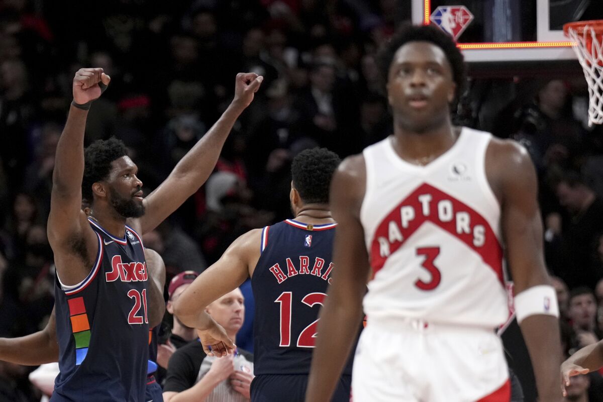 Toronto Raptors forward OG Anunoby (3) walks away as Philadelphia 76ers center Joel Embiid (21) celebrates the 76ers' overtime win with forward Tobias Harris (12) in Game 3 of an NBA basketball first-round playoff series, Wednesday, April 20, 2022, in Toronto. (Nathan Denette/The Canadian Press via AP)