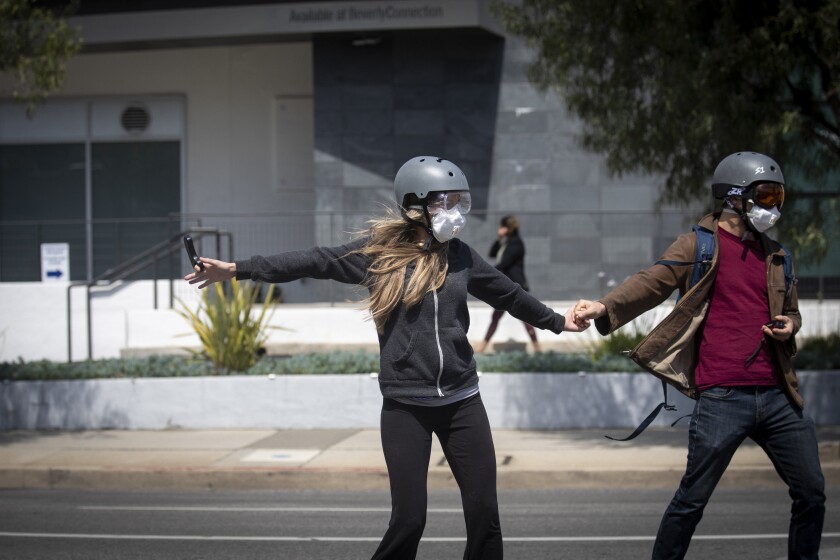 A couple wear masks, helmets and eye protection while skateboarding in Beverly Hills