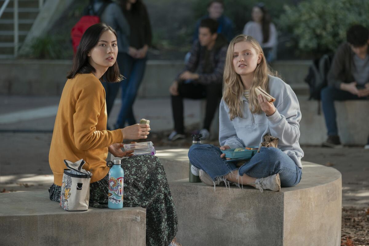Two girls sit on a high school campus eating lunch.