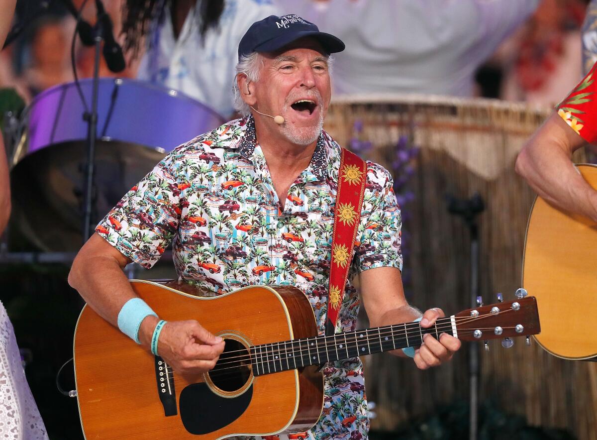 Jimmy Buffett performs with a guitar on a stage.