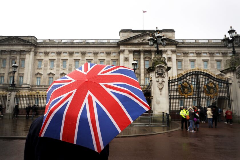 A tourist holds a Union flag umbrella outside Buckingham Palace in London, Tuesday, Jan. 14, 2020. In a statement issued on Monday, Jan. 13, 2020, Queen Elizabeth II says she has agreed to grant Prince Harry and Meghan their wish for a more independent life that will see them move part-time to Canada. (AP Photo/Kirsty Wigglesworth)