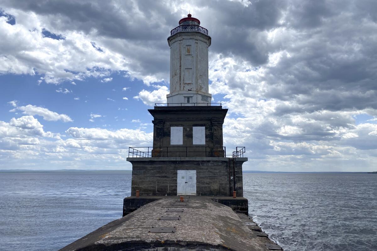 A lighthouse is seen against a backdrop of  ocean, sky and clouds.