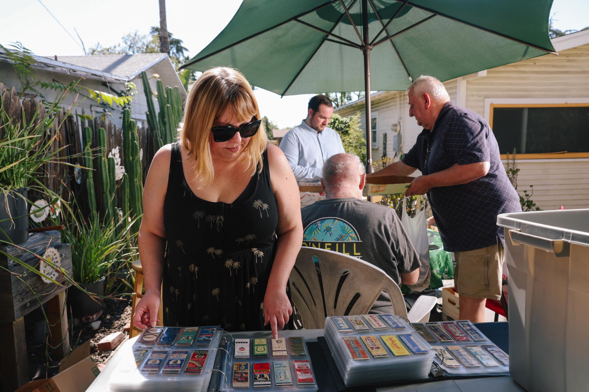 A woman stands outdoors leaning over a table that holds binders full of matchcovers.