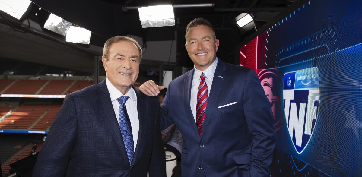 Two men in suits and ties smile in an empty stadium.