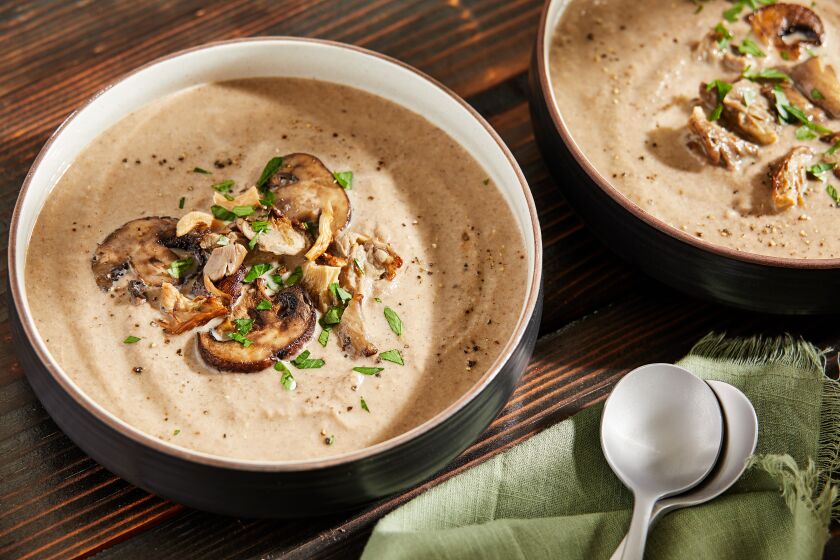 Two bowls of creamy mushroom soup topped with sliced mushrooms.