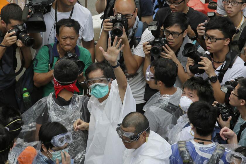 Activist Martin Lee, center, wearing goggles and a mask, waves to reporters outside government headquarters in Hong Kong.