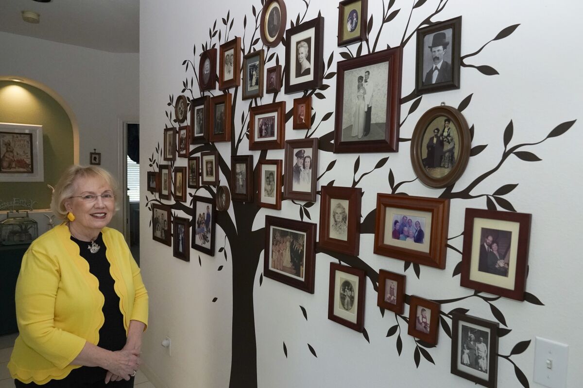 Elaine Powell, president of the Central Florida Genealogical Society poses with photos of her family tree on a wall at her home in Orlando, Fla., Wednesday, March 30, 2022. She plans to study the 1950 Census on its release at midnight on April 1. (AP Photo/John Raoux)