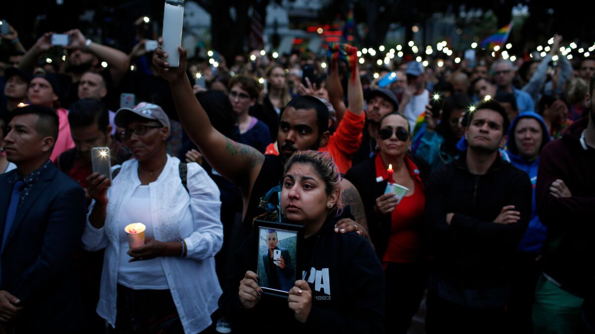 Alison Cossio, center, holds a photo of her friend, Christopher Sanfeliz, who was one of the victims of the Orlando shooting, during a candlelight vigil and rally at Los Angeles City Hall for the victims of Sunday's shooting massacre.