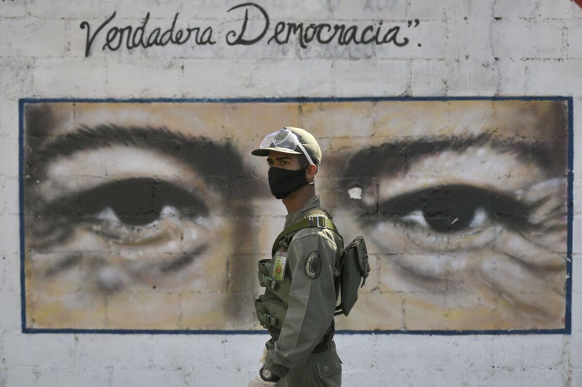 A soldier guards a voting poll at a school that has the eyes of the late President Hugo Chavez painted on a wall during elections to choose members of the National Assembly in Caracas, Venezuela, Sunday, Dec. 6, 2020. The vote, championed by President Nicolas Maduro, is rejected as fraud by the nation's most influential opposition politicians. (AP Photo/Matias Delacroix)