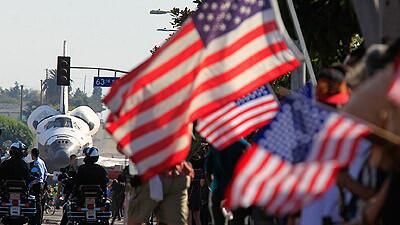 Flags are displayed as the space shuttle Endeavour moves along Crenshaw Boulevard. By Saturday evening, the craft was far behind schedule.
