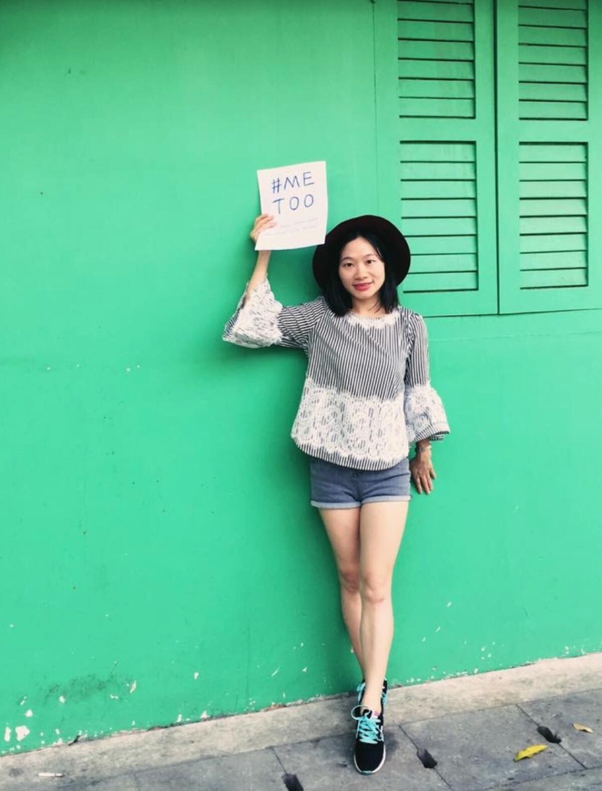 A woman in a hat holds up a sign that says #MeToo as she stands against a green backdrop