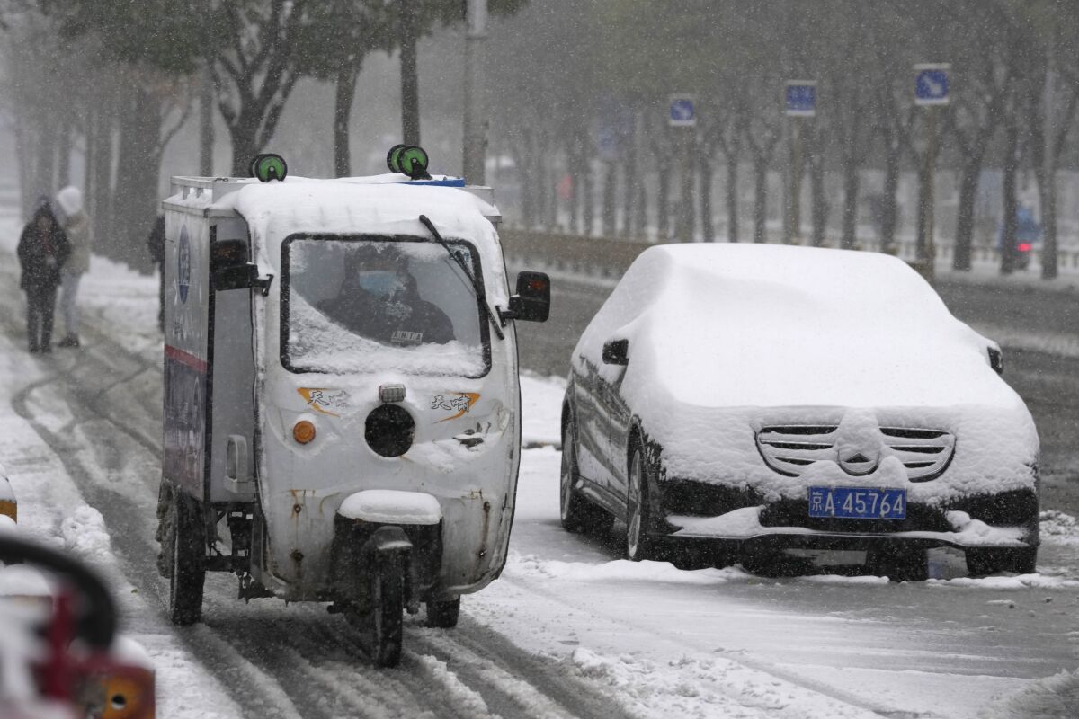 A delivery man moves past a car with a blanket of fresh snow in Beijing, China, Sunday, Nov. 7, 2021. An early-season snowstorm has blanketed much of northern China including the capital Beijing, prompting road closures and flight cancellations. (AP Photo/Ng Han Guan)