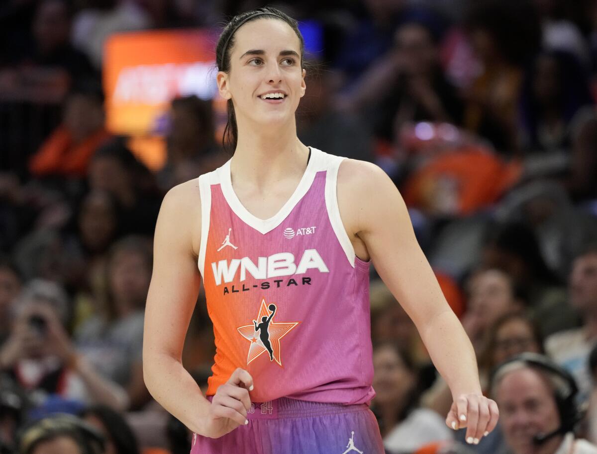 Caitlin Clark smiles and tugs on her All-Star jersey as she pauses on the court during the WNBA All-Star basketball game
